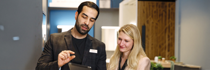 Mann zeigt Frau auf Tablet Badberatungsplanung in Badezimmerausstellung, Verkaufsberater erklärt Sanitärobjekte und Materialien
