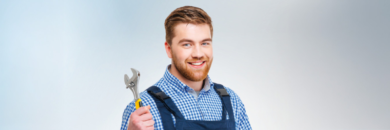 junger Handwerker in Latzhose mit Schraubenschlüssel lächelnd, Porträt für Handwerker finden 3x1